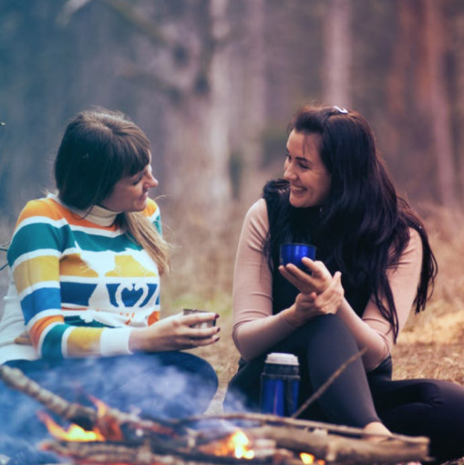 two women sitting by a fire enjoying a warm beverage and chatting